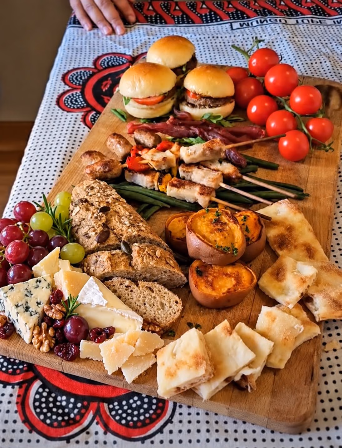 Grazing board with brioche sliders, chicken skewers, roast sweet potato, seeded loaf, focaccia, cheeses, grapes and vine tomatoes