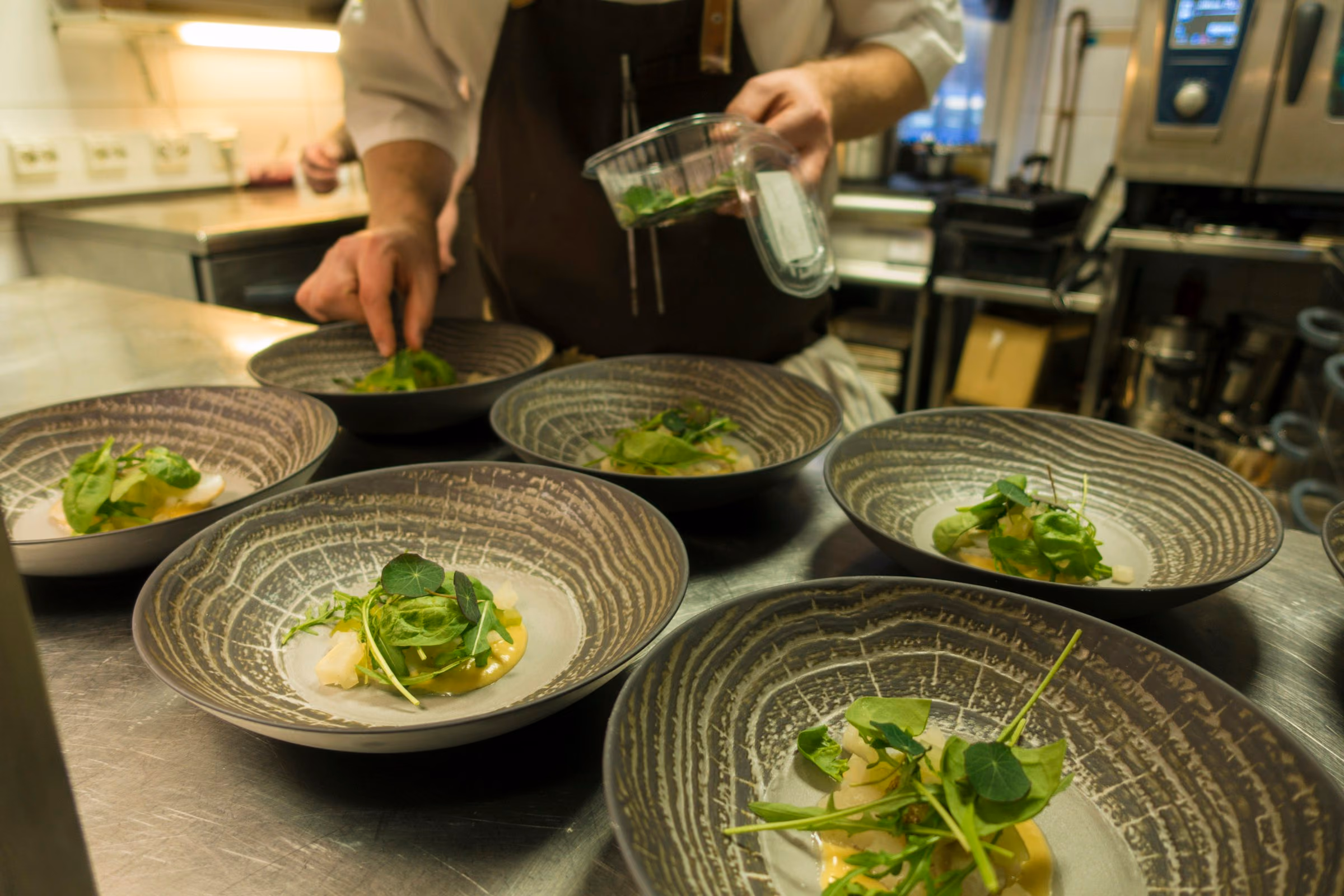 Green starters plated in stoneware bowls at the pass
