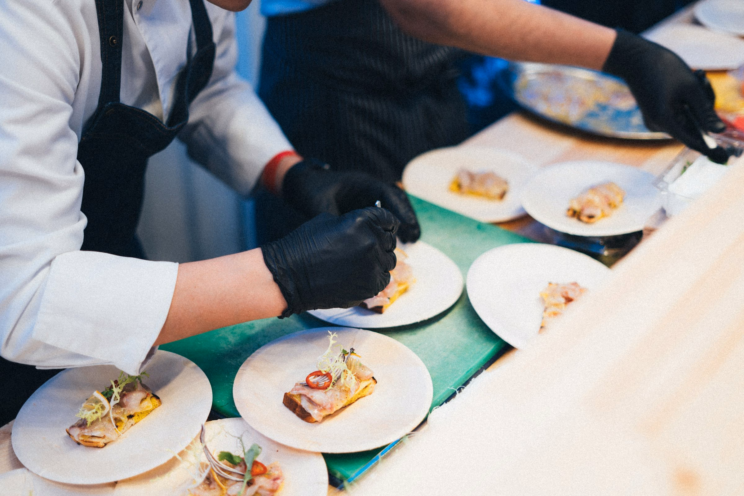 Brigade in black gloves plating fish courses in a line