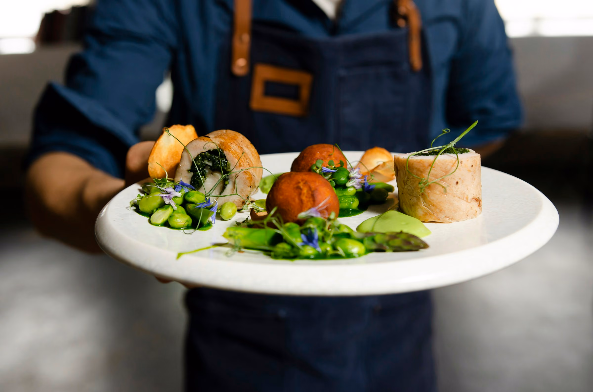 Server in a navy apron presenting a plated starter