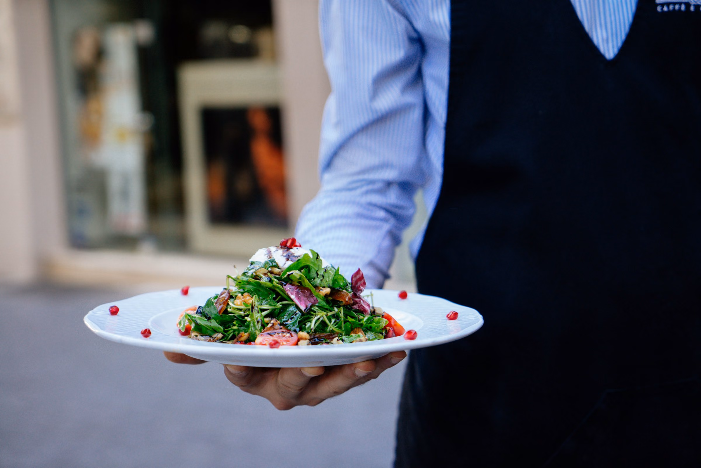 Server in a navy apron carrying a plated salad