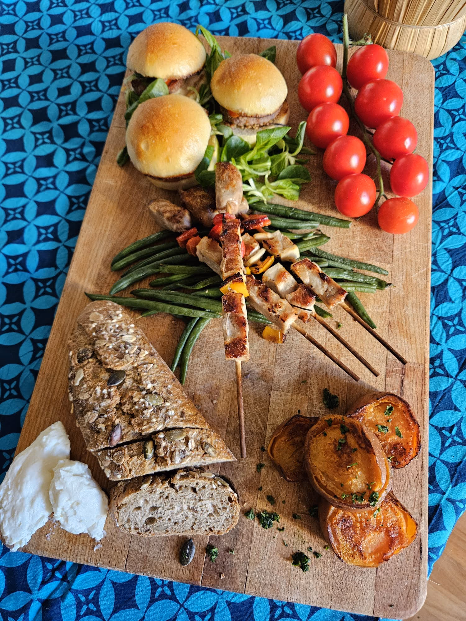 Sharing board with brioche sliders, grilled chicken skewers, seeded bread and vine tomatoes