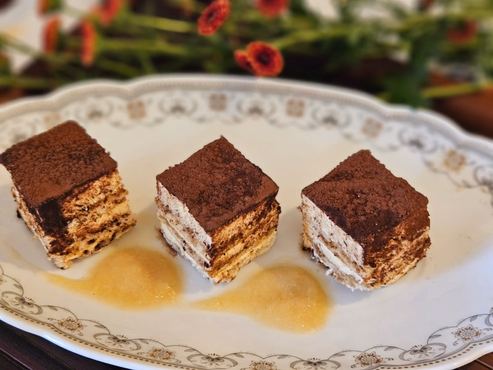Three squares of tiramisù dusted with cocoa on a vintage plate